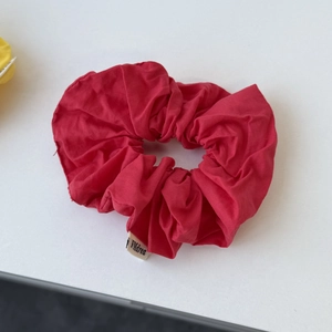Detail of red oversized scrunchie in thick cotton fabric with a white woven brand label