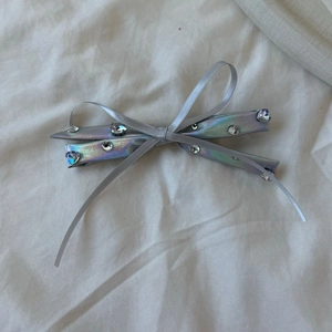 Detail view of silver PU leather bow hair clip with sparkling rhinestones on white fabric