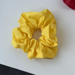 Detailed close-up of vibrant yellow cotton scrunchie with elastic folds and branded label