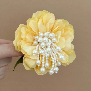 Detail of yellow fabric flower hair clip with pearl tassels and a green leaf embellishment