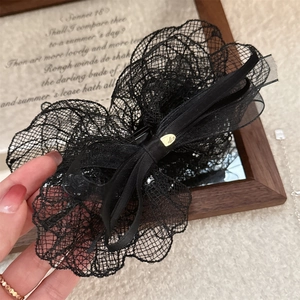 Close-up of a large black lace bow hair clip with a golden metal logo buckle detail