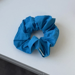 Detailed close-up of a navy blue fabric scrunchie with soft pleated texture and label
