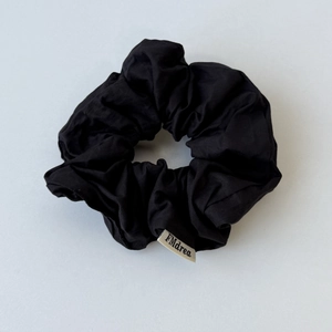 Macro detail of a black fabric scrunchie featuring a beige FMdrea brand logo label