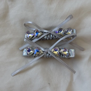 Close-up of two silver ribbon bow hair clips with shimmering AB rhinestone centers