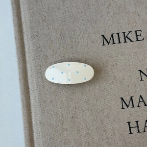 Detail view of oval hair clip with light blue polka dots on a cream acetate surface