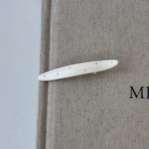 Detail view of cream white oval hair clip with light blue polka dots on linen fabric