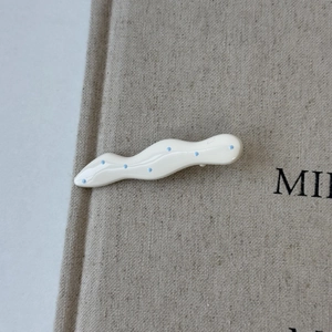 Detail of cream wave hair clip with blue polka dots and a high-gloss polished finish