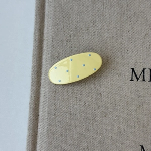 Chic oval hair clip in bright yellow with blue polka dots on a natural fabric background