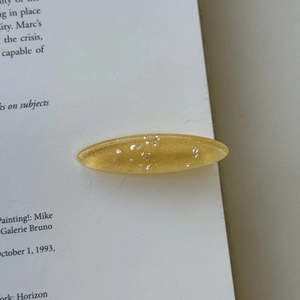 Detail of yellow glitter resin oval hair clip on an open book for a sweet aesthetic style