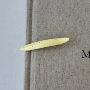Macro detail of a pale yellow duckbill clip with blue polka dots on linen fabric texture