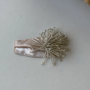 Macro view of handmade silver beaded champagne satin hair clip with 3D fireworks design