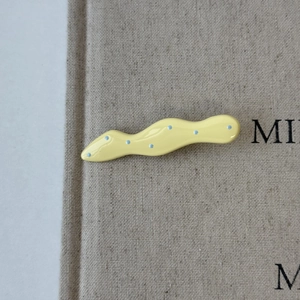 Detailed view of wave-shaped yellow hair clip with blue polka dots on grey fabric