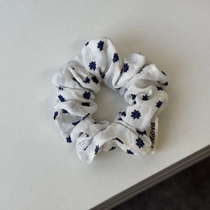 Detailansicht eines weißen Haargummis mit blauen Blumenmustern und kleinem Markenetikett