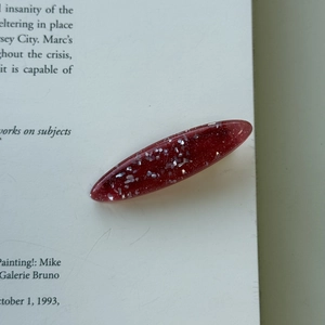 Close-up of translucent burgundy hair clip with glitter sequins on a white book page