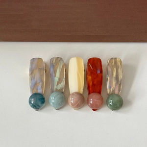 Five assorted ink marble resin hair clips with spherical accents on a wooden background