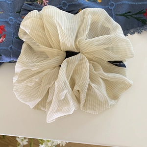 Dettaglio di scrunchie in organza a quadretti beige con trama del tessuto e etichetta
