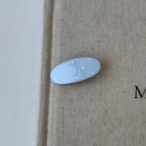 Detailed view of light blue oval hair clip with white polka dots on linen fabric