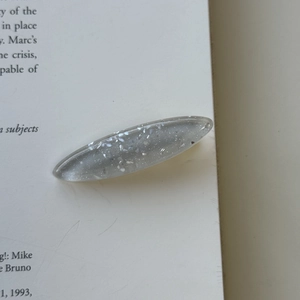 Close-up of a translucent grey resin hair clip with silver glitter and sequins on a book
