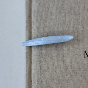 Close-up of light blue resin hair clip with white polka dots on a textured background