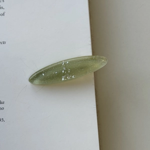 Close-up of translucent olive green oval hair clip with fine glitter on a book page