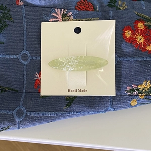Dettaglio di un fermaglio ovale verde chiaro con texture a conchiglia su supporto