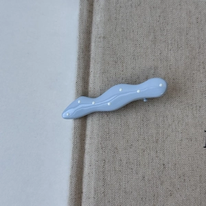 Detail shot of light blue wavy hair clip with white polka dots and smooth resin finish