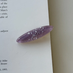Close-up of a purple translucent hair clip with silver glitter on an open book