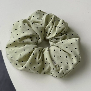 Détail d'un chouchou en tissu vert menthe avec motifs de petits cœurs noirs et étiquette
