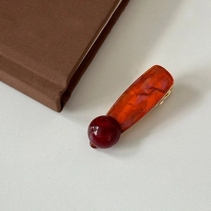 Detail of amber acetate hair clip with red marble bead decoration on textured surface