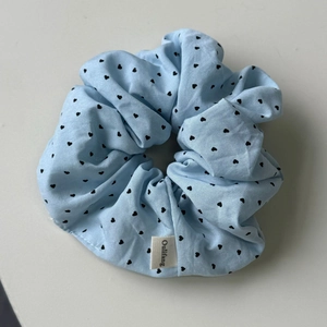 Gros plan du chouchou en tissu bleu clair avec motifs cœurs noirs et étiquette