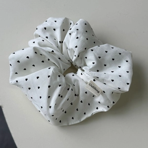 Détail d'un chouchou blanc avec motifs de cœurs noirs et étiquette de marque