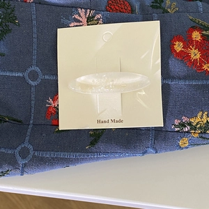 Dettaglio del fermaglio ovale in resina bianca con glitter su fondo floreale blu ricamato
