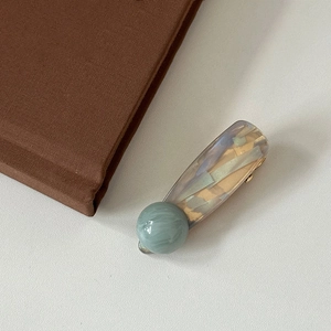 Macro shot of marble texture hair clip with pastel green sphere and golden metal clasp