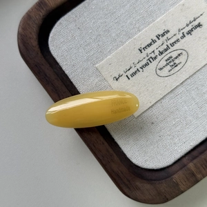Fermaglio per capelli ovale in acetato giallo con scritte dorate su vassoio in legno