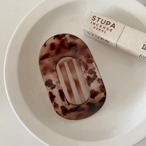 Flat round tortoiseshell hair claw clip displayed on a white ceramic plate in macro detail