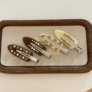 Set of four floral rhinestone hair clips in dark brown and cream on a wooden tray