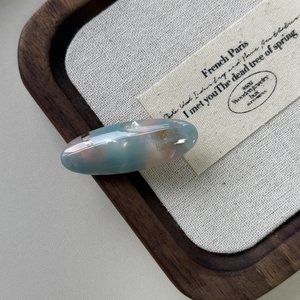 Dettaglio macro di un fermaglio ovale in acetato con trama marmorea e scritte dorate