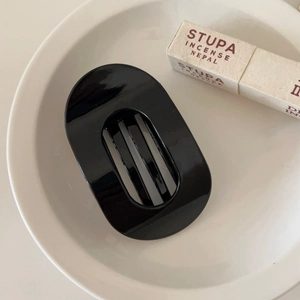 Detailed view of a black oval flat hair claw clip with unique vertical grid design on a plate