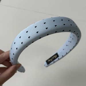 Détail d'un serre-tête rembourré bleu clair avec motifs cœurs noirs et étiquette