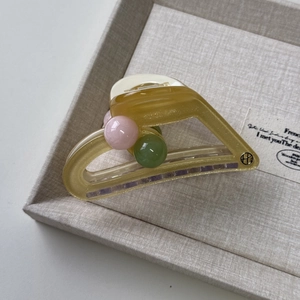 Detail view of yellow jelly shark hair clip with colorful beads on a grey display tray
