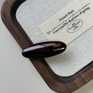 Dettaglio del fermaglio ovale in acetato marrone rossiccio con scritta oro France Handmade
