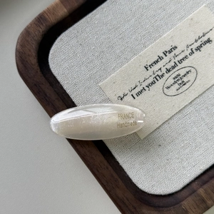 Dettaglio del fermaglio ovale in acetato crema con scritta dorata France Handmade