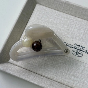Detail of jelly-colored hair claw with cream finish, marble beads, and gold logo charm