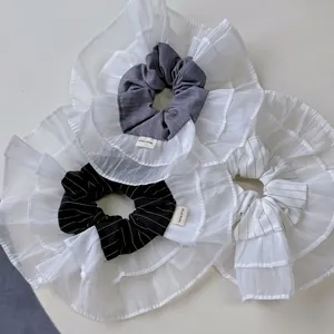 Three-color striped scrunchies with white ruffle edges and handmade labels in a flat lay view