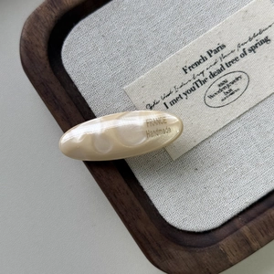 Dettaglio molletta ovale in acetato con scritta dorata France Handmade e trama in mica lucida