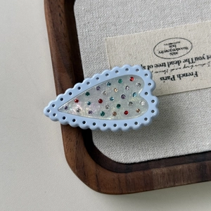 Close-up of heart-shaped light blue hair clip with colorful rhinestones on linen