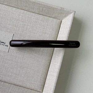 Detailed close-up of slim dark brown acetate hair clip with gold lettering on tray
