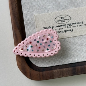 Detailed top view of pink heart hair clip with colorful rhinestones on a wooden tray
