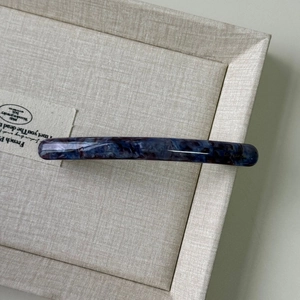 Detail of blue purple marbled acetate hair clip with elegant glossy texture on beige tray