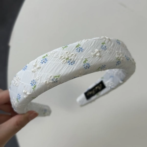 Detailed macro shot of white fabric headband featuring blue floral embroidery and 3D texture